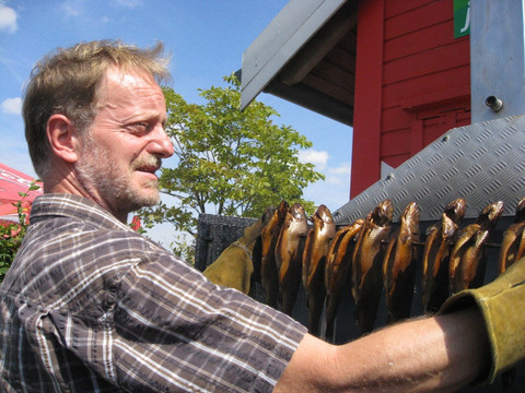 Ein Mitarbeiter des Pier 1 Biergartens betrachtet Räucherfische am Spieß, Gastronomie, Kulinarik