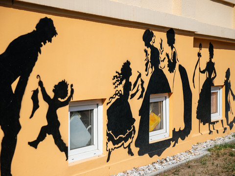 Blick auf eine sandfarbene Hauswand, die mit den schwarzen Silhouetten historischer Familien geziert wurde; Graffiti