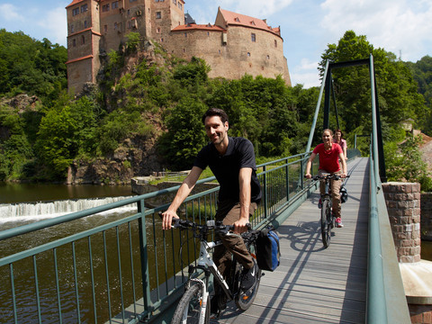 Zwei Radfahrer überqueren eine Brücke über die Zschopau, im Hintergrund Burg Kriebstein, Radwanderwege