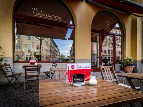 Blick auf einen Holztisch des Freisitzes vor der Eisträumerei Leipzig, mit Blick auf die Fenster der Eisdiele im Hintergrund, eisdiele, cafe, freisitz