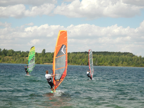 Drei Windsurfer stehen auf ihren Boards bei Wellengang auf dem Schladitzer See