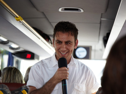 Ein Mann im Bus der Stadtrundfahrt der Comedytour mit Mikrofon in der Hand
