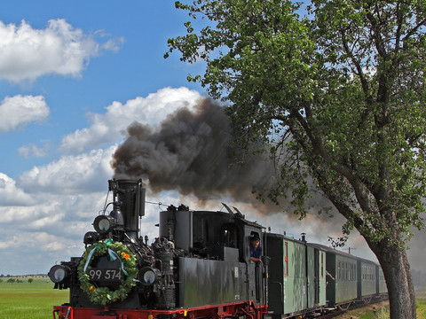 Der Dampfzug der Döllnitzbahn fährt zwischen Oschatz, Mügeln und Kemmlitz / Glossen und stößt dabei dunkle Rauchwolken aus