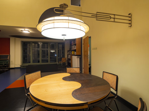 Ein runder Esstisch aus Holz wird beleuchtet von einer großen Lampe im Bauhausstil
