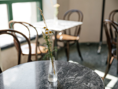 Fotografie der Tischdeko im INO Café; Sträucher in Glasvase; im Hintergrund sind weitere Tische im hellen Café zu erkennen, Gastronomie, Cafe, freizeit