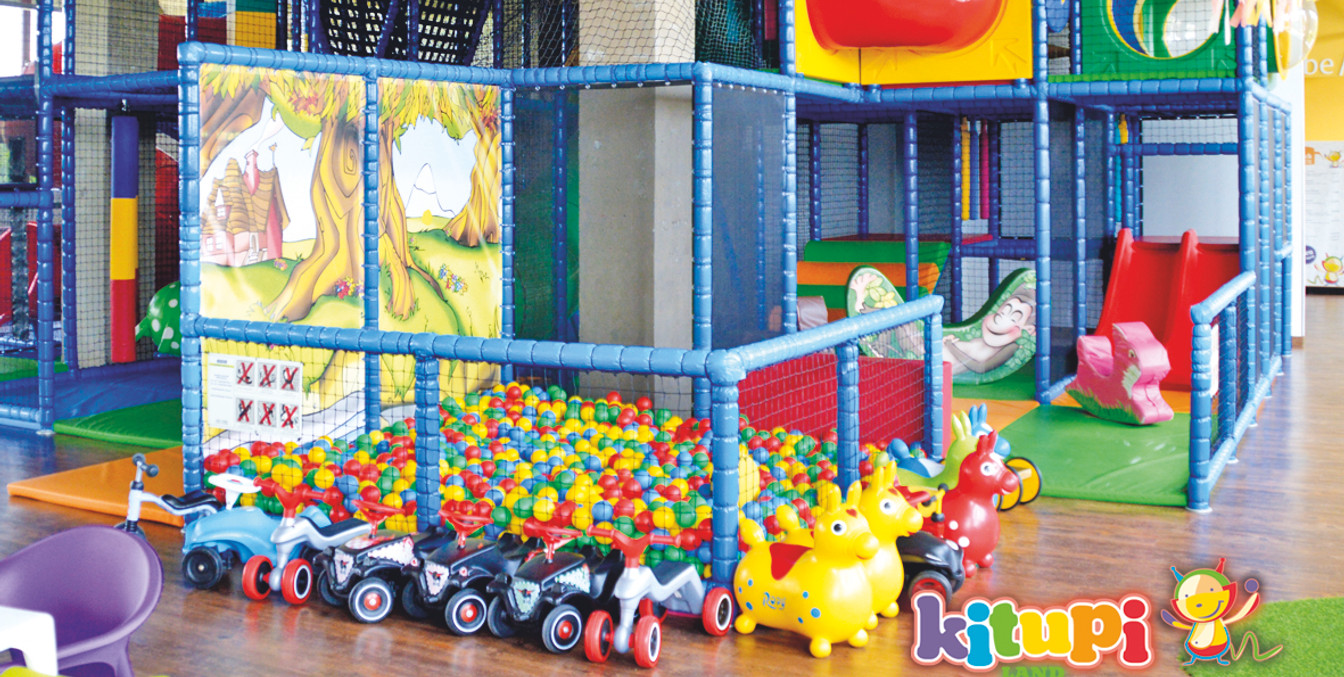 Zu sehen ist ein buntes Kletterkonstrukt für Kinder mit einem Bällepool, Bobbycars und weiteren bunten Spielzeugen, Freizeit-Indoorspieplatz-Ferien