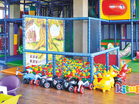 Zu sehen ist ein buntes Kletterkonstrukt für Kinder mit einem Bällepool, Bobbycars und weiteren bunten Spielzeugen, Freizeit-Indoorspieplatz-Ferien