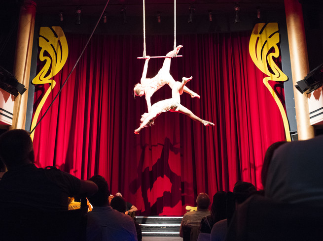 Blick durch die Zuschauerreihen auf die Bühne im Krystallpalast Varieté auf der zwei Artisten an einem Trapez hängen und performen