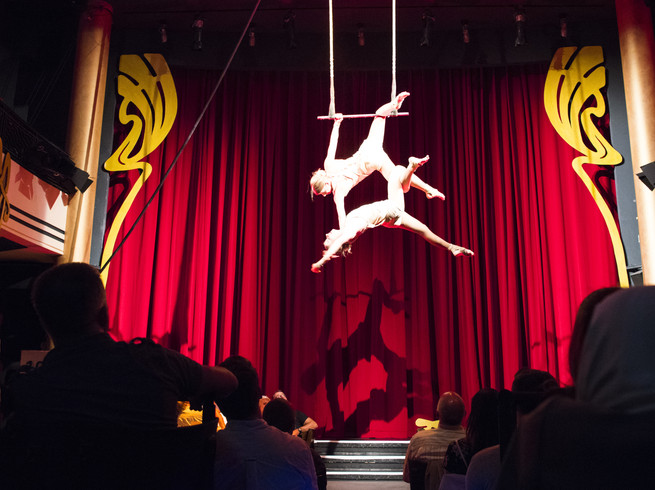 Blick durch die Zuschauerreihen auf die Bühne im Krystallpalast Varieté auf der zwei Artisten an einem Trapez hängen und performen