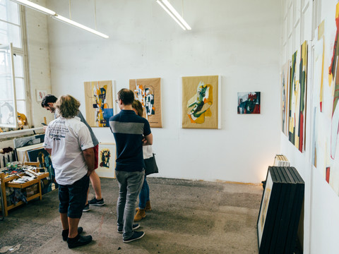 Blick in einen hellen, minimalistischen Galerie-Raum und auf einige Besucher, die die bunten Wandgemälde der Ausstellung ansehen, Leipzig und Region 