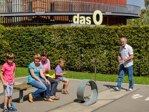 Familie spielt Minigolf, Im Hintergrund die Multifunktionshalle "das O", Freizeit, Tierpark, Familienausflug