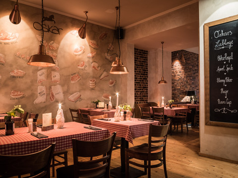 Dargestellt ist der gemütliche Gastraum im schummrigen Licht und dunklen Holzmöbeln sowie rot-weiß karierten Tischdecken, Gastronomie-Bar-Restaurant-Freisitz 