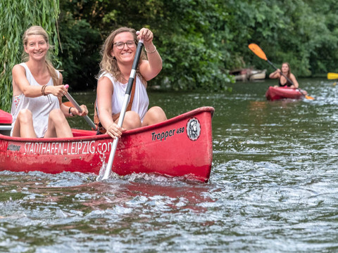 Zwei Frauen paddeln in einem roten Kanu auf dem Wasser auf Leipzigs Wasserwegen, Wassersport in Leipzig